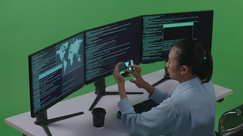 Femme développeuse travaillant avec un téléphone portable tout en écrivant du code avec plusieurs ordinateurs sur écran vert