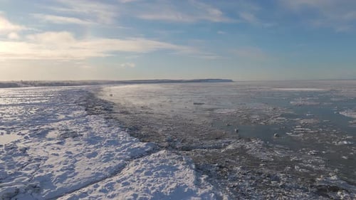 Wide Forwarding Drone Shot over Large Frozen Body of Water with Snow on top, Beautiful Sky