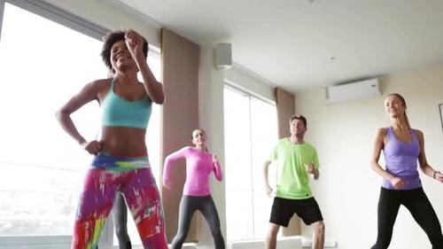Smiling zumba group having fun dancing with instructor in gym or studio