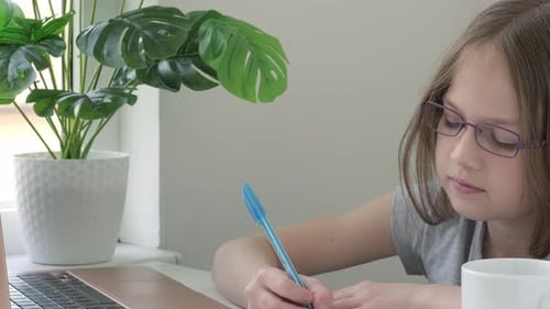 Young Girl Writing in Notebook at Table