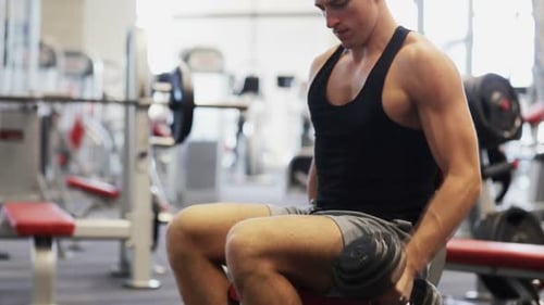 Young man flexing muscular biceps holding dumbbell during gym workout
