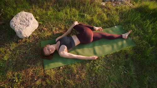 Femme faisant une pose de yoga en position couchée dans la forêt, lever du soleil dans la nature
