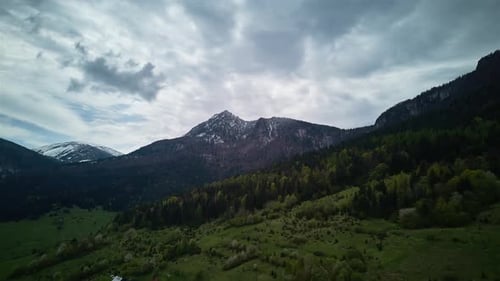 Hyperlapse aus der Luft: Frühling, Alpen, Berge, flauschige Wolken, grüne Wiesen und blühende Bäume im Tal.