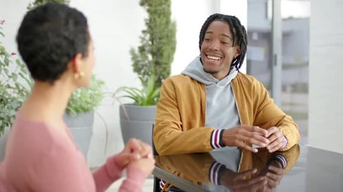 Homme afro-américain penché en avant expliquant avec les paumes levées à côté d'un pair à table sur la terrasse