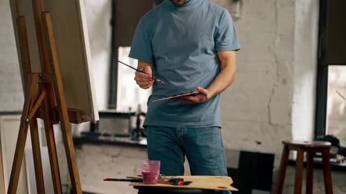Nahaufnahme in einem Kunststudio: Ein Künstler in einem blauen T-Shirt arbeitet an einem Gemälde