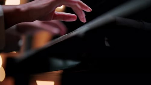 Close up of a woman's hands playing the piano with blurry lights on the background