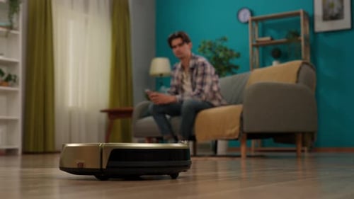 Young Adult Relaxing as Robot Vacuum Cleans Floor