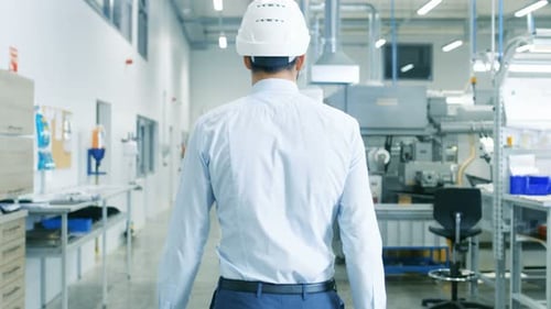 Back View Footage of the Chief Engineer in the Hard Hat Walking Through Light Modern Factory While