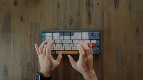 Hands Typing on Colorful Keyboard on Wooden Desk