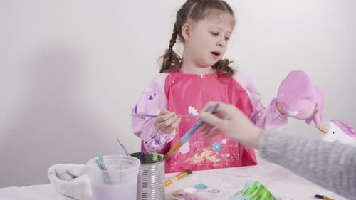 Kleines Mädchen bemalt Pappmaché-Figuren mit Acrylfarbe für ihr Homeschooling-Kunstprojekt