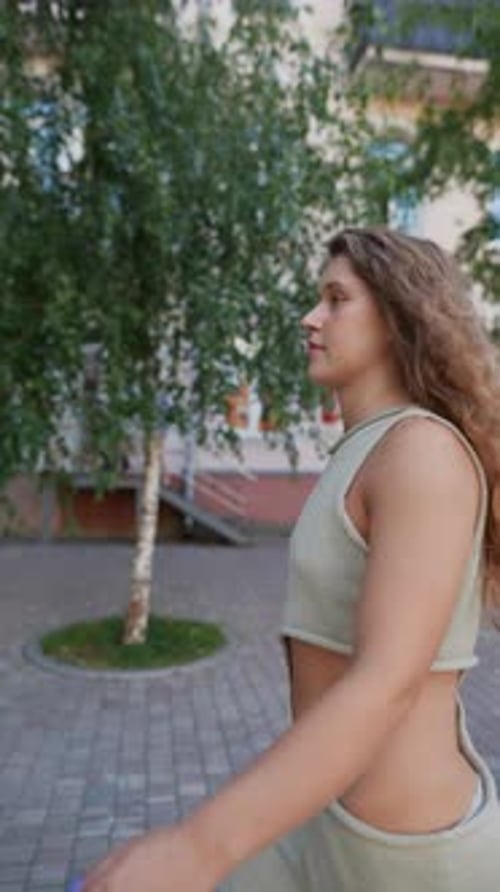 Amidst the City Streets on a Summer Day a Girl with Curly Hair is Taking a Leisurely Walk