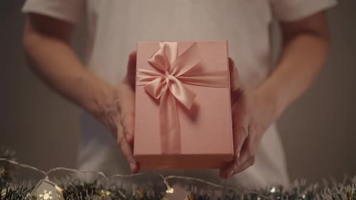 Front View of Man Presenting Beautifully Wrapped Pink Gift Box with Ribbon and Bow Against Sparkling