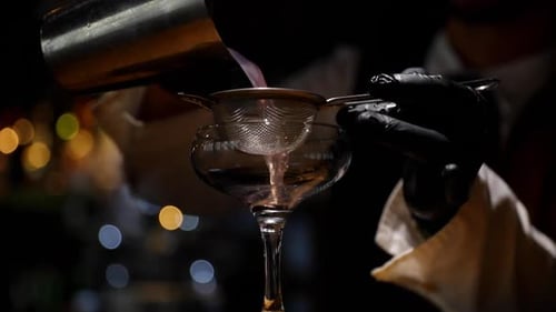 Bartender pouring drink from shaker into glass over deep ready to serve final drink closeup view of