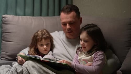 Father Reading Story to Young Daughters on Couch