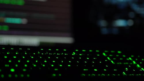 Concept de cybersécurité. Gros plan du clavier éclairé en vert dans une pièce sombre avec le code du hacker clignotant
à l'écran