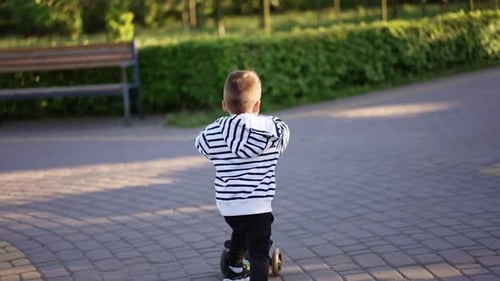 Following a little boy riding his scooter in the park.