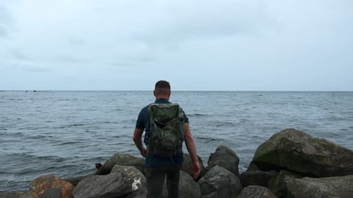 Man walks on stone coast on background of sea. Clip. Man walks on stones of sea
