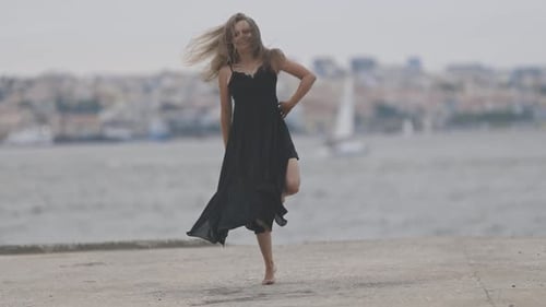 Cute Smiling Woman in Black Dress Dancing on the Promenade in Cloudy Weather