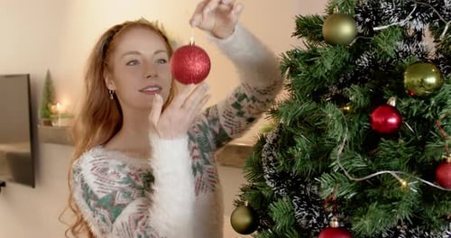 Woman Decorating Christmas Tree with Ornaments at Home