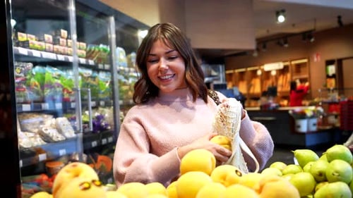 Happy Young Woman Choosing Fresh Fruit at the Grocery Store