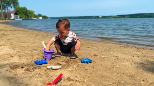Adorable Caucasian baby boy playing with bucket and shovel on the beach.