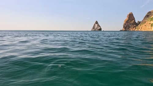Sea Water Surface Camera Flies Over the Calm Azure Sea with Volcanic Rocky Shores on Background
