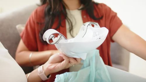 Diverses amies ouvrent une boîte de livraison sur le canapé et inspectent le masque facial à LED blanc pour vérifier son ajustement