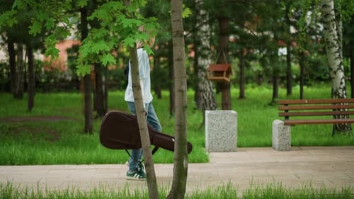 Man Walking with Guitar Case Guitarist Moving Along Park Pathway with Equipment Man with Guitar in