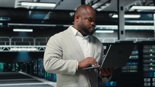 Technician Walking in Data Center Using Laptop to Check Hardware
