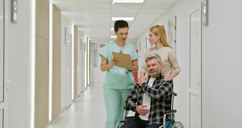 MiddleAged Man in Wheelchair with Nurse and Companion in Hospital