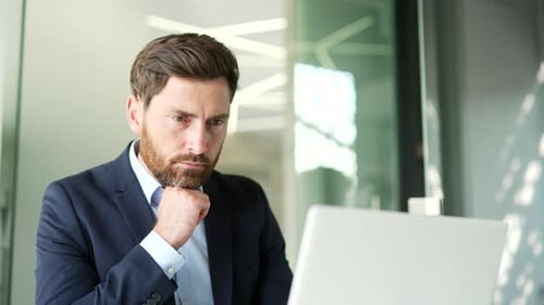 Serious thoughtful businessman in formal suit works on a laptop sitting at a workplace in business