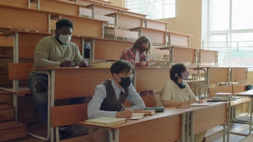 Students Writing at Desks in Masks in Classroom