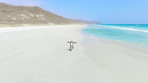 Aerial View of a Young Woman Walking Along the White Sand Beach with Turquoise Water and Mountains