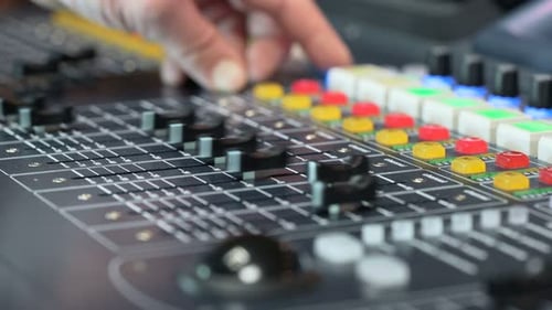 Hand adjusting audio console knob in colorful professional recording studio