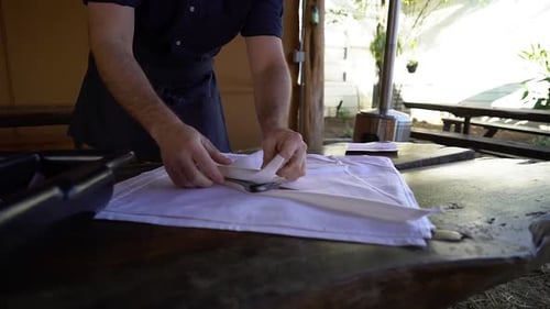 Caterer Rolling Silverware into Napkin in Restaurant