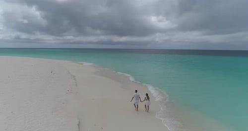 Aerial view of romantic couple dressed in white walking holding hands on a white sand Caribbean Isla