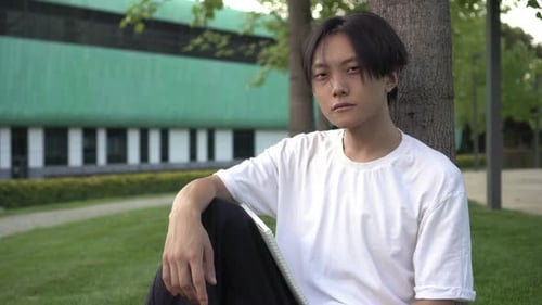 Young Adult Sitting with Tablet by Tree