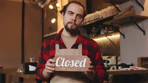 Barista Holds Closed Sign at Cafe After a Day of Serving Coffee and Roasting Beans for Customers in