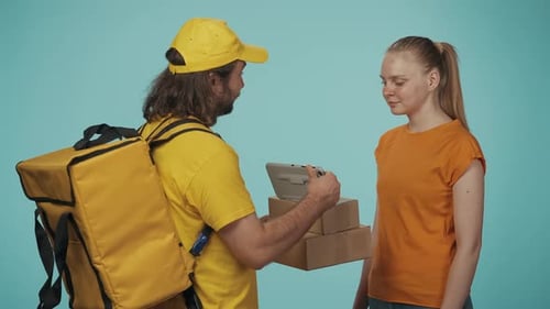 Delivery Man in Yellow Uniform with Portable Backpack Gives a Girl Customer Packages She Signs the