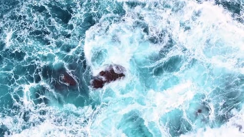 Waves crash against rocks in clear blue ocean water during sunny afternoon