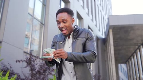 Excited Young Adult Counts Stack of Cash in City