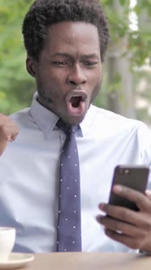 African Businessman Cheering Success on Smartphone Sitting in Outdoor Cafe, Vertical Video