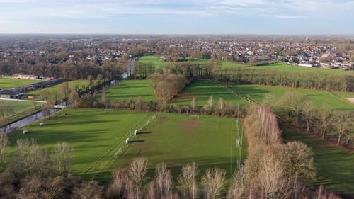 Aerial view of rural fields with crop rows, tree shadows, canal, and farm buildings sunlit landscape