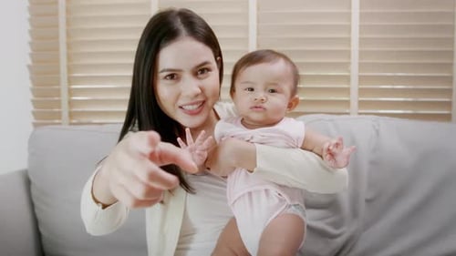 Woman Holding Baby on Sofa Waving