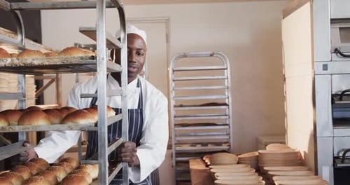 Happy diverse bakers working in bakery kitchen, holding baking sheets with rolls in slow motion