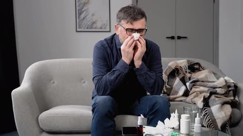 Adult Man Blowing Nose on Couch at Home
