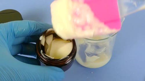 vue d'une scène de laboratoire de cosmétiques où un opérateur ganté utilise une spatule pour emballer soigneusement un sachet