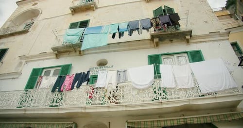 Laundry Hangs From Ornate Balconies with Green Shutters on a Weathered Building in Italy