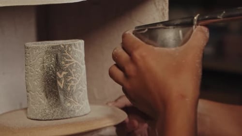 Pottery in the Studio Potter pulvérise manuellement de la peinture en poudre blanche sur le gobelet en argile en soufflant
