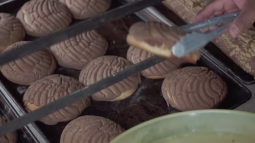 A person uses tongs to grab a freshly baked pastry off of a baking sheet in a bakery.